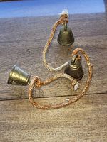 Overview of the three small vintage brass bells connected by a braided orange and white rope, showing the etched designs and braided cord.