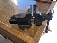 Black solid cast iron vintage table vice viewed from side, showing screw mechanism and jaws.