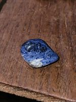 Polished blue sodalite stone specimen showing vibrant blue with black and white inclusions on wooden surface.