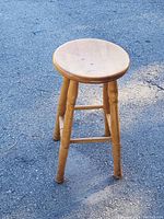 Photo showing the full view of the hand-turned solid maple wood stool on pavement, with visible wear on legs.