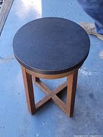Full view of solid oak round top table on blue floor, showing dark top and X-shaped base support.
