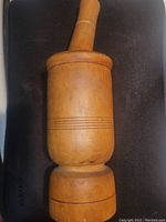 Photo showing the upright wooden mortar and pestle set, with clear view of the carved decorative lines on the mortar.