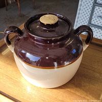 Stoneware bean crock 12 inches tall, two-tone with dark brown top and beige bottom, with lid on.