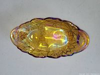 Top view of oval carnival glass candy dish showing sunflower pattern and iridescent marigold amber color with two handles.