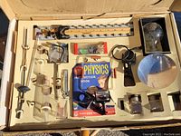 Full contents of vintage 1950s Gilbert Physics Set including instruction book and various glassware, optics, and accessories arranged in original box insert