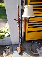 Full view of the vintage wooden standing lamp showing the turned wood design and tripod base beside a yellow tool chest and outdoor flowers.