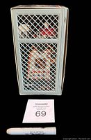 Front view of the plastic locker box with cards visible behind lattice, displayed alongside a marker and auction lot number card for scale.