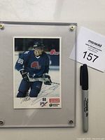 Front view of Joe Sakic autographed Quebec Nordiques promo card in Lucite display holder alongside a Sharpie for scale.