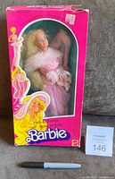 Front view of the Barbie doll in original box with pink feather boa and shiny pink dress. Box shows wear and tear.