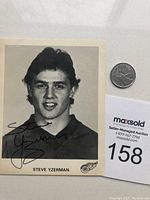 Full view of Steve Yzerman autographed black and white photo with a measuring coin for scale, showing the front with autograph and printed name on bottom edge.