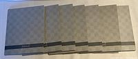 Seven hardcover journals laid out side by side, showing consistent gray checkered pattern covers with a darker band at the bottom labeled 'journal'.