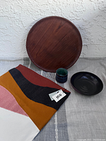 Four items arranged on a gray surface against a white textured wall including the lazy susan tray propped up, pottery pieces, and cushion cover folded, showing the lot contents.
