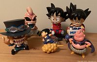 Six Dragon Ball Z collectible figures arranged on a flat surface. Characters include Goku in different poses, Majin Buu, and others, showing size variation and detailed features.