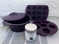 Purple silicone steamer, donut pan, muffin maker with unopened hot chocolate mix in front on grey surface and white wall background.