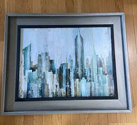 Framed cityscape art print showing tall buildings in grey and turquoise tones, captured from above looking straight onto the framed art.