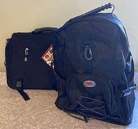 Both the black shoulder bag with Pak branding and the black Swiss Gear backpack shown side by side on a surface.
