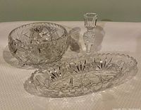 Set of three crystal items on white textured fabric: round footed bowl, candlestick, and oval dish, showing shape and patterns.