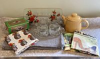 Lot composition showing yellow Sadler teapot, grey placemats, clear glass serving dish with floral design, green decorative tea tin, four Nabisco collectible cups, and vintage tea towels.
