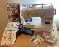 Photo of Kenmore sewing machine, sewing patterns, magazines and various sewing accessories arranged on a wooden table.