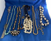 Photo showing full set of 9 distinct vintage costume jewelry necklaces laid on blue cloth.