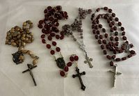 Four vintage rosary bead sets laid out on white fabric, showing variation in bead colors and styles, each with crucifixes and religious medals.