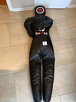 Full view of the black training dummy lying flat on floor, arms crossed across chest, Bestzo logo visible