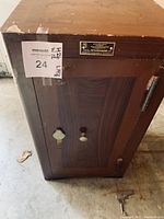 Front view of the antique safe showing wooden door with two locking knobs and Russian metal plate above. Two keys visible on the floor in front.