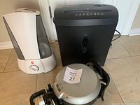 Front angle of all three appliances: white humidifier, black paper shredder, and silver waffle maker with controls visible