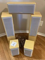 Front view of five speakers and wiring showing two large floor-standing speakers, one center speaker, and two smaller bookshelf speakers arranged on floor with wiring bundled in center.