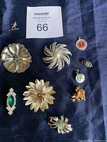 Full view of all brooches and charms on a dark blue textile background with auction label