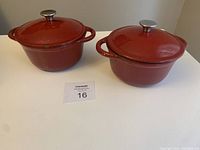 Two red cast iron Dutch ovens with lids shown on white surface.