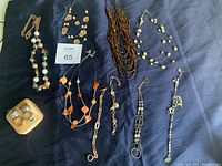 Photo showing five necklaces, including pearl bead strand, multi-strand brown beads, gold-tone chain with beads, displayed on a dark fabric.
