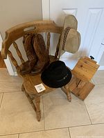Lot items on a wooden chair against a white door background, showing hats, boots, chair, and wood easel.