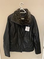 Front view of the women's black leather jacket with fur collar, hanging on a white hanger, showing zip-front closure and pockets.