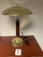 Full view of the desk lamp showing brass shade, red marble effect column, and base with cord and dimmer switch coiled beside.
