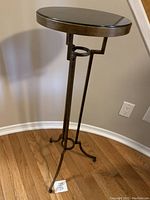 Full view of a tall plant stand featuring a black marble top and iron legs on a hardwood floor.