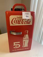 Front view of red mini Coca-Cola fridge showing vintage branded graphics, handle and carry handle on top.