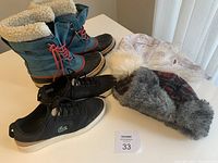 Photo of Sorel boots, Lacoste shoes, and two winter hats arranged on a white table.