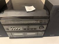 Front view of Panasonic audio system with turntable, tuner, control panel, and cassette decks, showing control buttons and knobs, with speakers on each side.