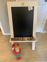 Wooden framed chalkboard showing star cutout and base shelf holding various items with a Barbie doll seated beside it
