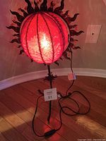Red fabric boho table lamp lit, showing the glowing shade, metal sun motif, and tripod base.