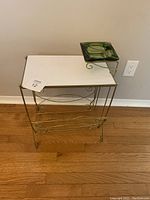 Full view of metal framed magazine holder with white base and attached green glass ashtray on top.