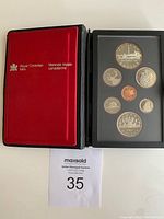View of the opened red velvet and black leather case showing seven 1984 Canadian coins held in place under a protective clear cover