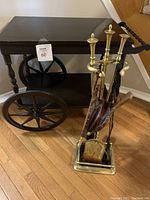 Full view of wooden tea cart and brass fireplace tool set with leather fireplace bellow