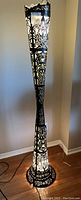 Full height view of the tall torch-shaped aluminum floor lamp, showing decorative pierced metalwork and base.