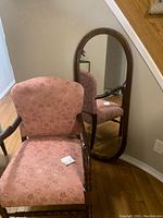 Victorian style armchair with pink floral upholstery and wooden carved arms next to a wooden oval mirror leaning against the wall.