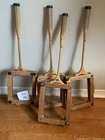 Four vintage wooden racquets with wooden handles and rectangular frames, grouped standing against a wall.