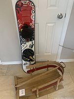 Photo showing the full wooden sled and snowboard standing against a door, capturing size and condition.