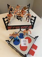 Photo showing multiple WWF wrestler action figures positioned inside two miniature wrestling rings on a white table.