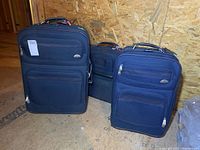 Three navy blue Samsonite wheeled suitcases grouped together on plywood floor with unfinished OSB wall in background.